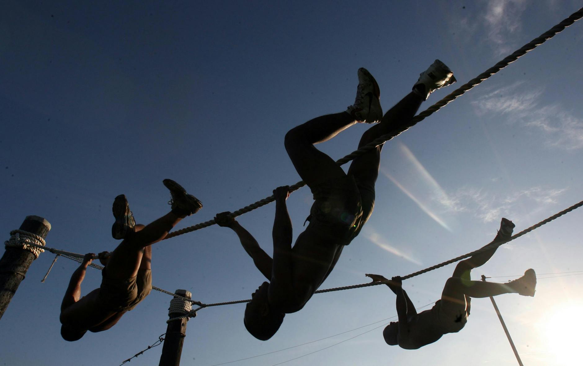 three man climbing on rope under the sunset